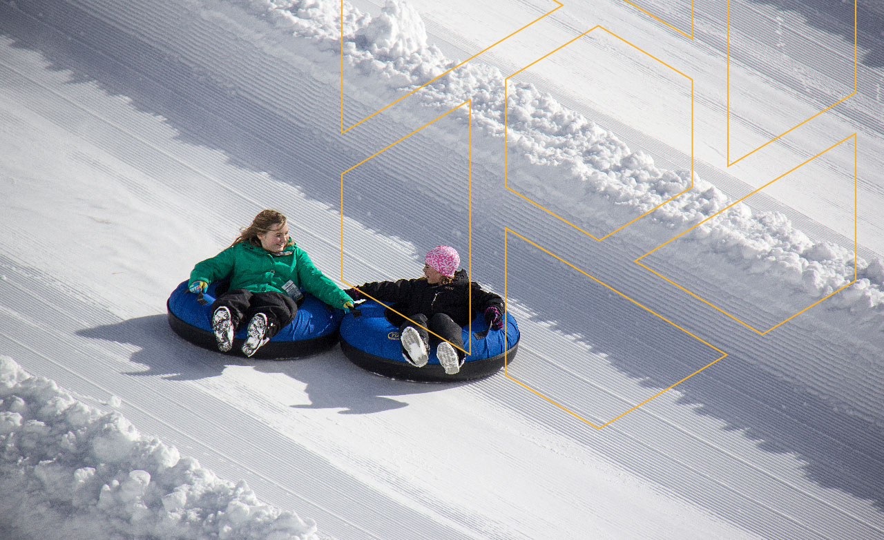 two young girls holding eachother's intertubes, tubing down a run at Mount Washington